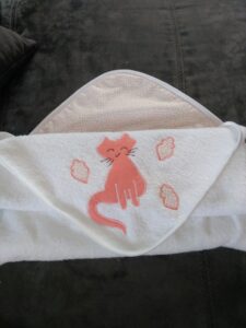 sortie de bain blanche et rose orangé pliée avec motif chat